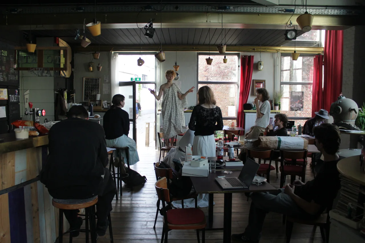 Spelers repeteren tussen tafels en stoelen in een café.